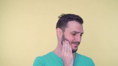 Diş ağrısı olan, acı çeken ve yanağına dokunan genç adamın yakın çekimi.