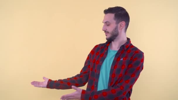 Bearded man presenting with hands at invisible product, isolated on yellow background — Stock Video