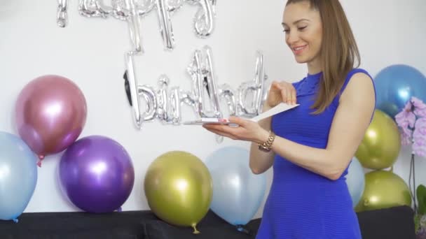 Έκπληκτη Νεαρή γυναίκα ανοίγει ένα δώρο γενεθλίων στο πάρτι γενεθλίων με πολύχρωμα μπαλόνια — Αρχείο Βίντεο
