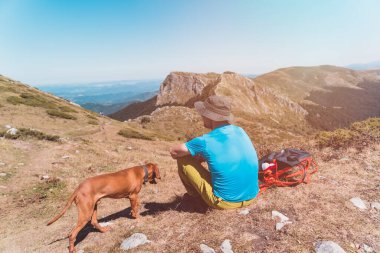 Dağ manzarasını aşan ve Vizsla köpeğiyle yürüyüş yapan