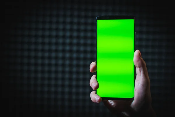 Espaço de cópia segurando telefone celular preto com uma tela verde, isolado em um fundo escuro embaçado — Fotografia de Stock