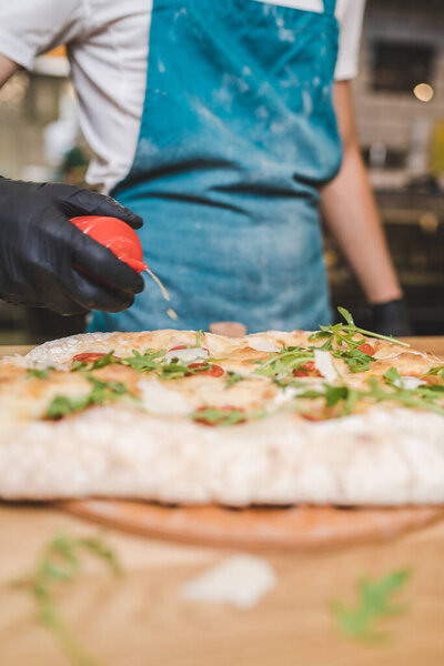 Homemade fresh Pizza with bacon, arugula, parmesan and cherry tomatoes. Chef hands putting olive oil and spices on pizza, close shot. High quality photo