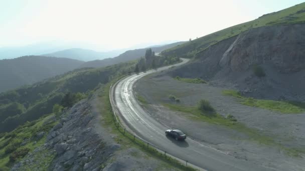 Um carro preto dirigindo na estrada ensolarada montanha — Vídeo de Stock
