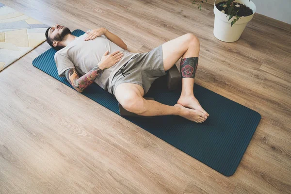 Fiatalember meditál és mélyeket lélegzik jóga szőnyegen. Férfi csinál rekeszizom légzés gyakorlat Stock Kép