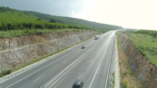 Vista aérea da rodovia entre colinas verdes com tráfego de verão movimentado em dia quente — Vídeo de Stock