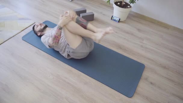 Homme à Pavanamuktasana pose dans un tapis de yoga. Homme étirant les muscles à la maison — Video