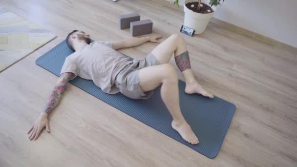 Jongeman ontspannen en doen liggend spinale twist yoga pose thuis — Stockvideo