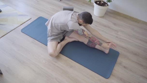 Adam yoga yapıyor, ayak parmağını sol bacağında tutuyor. Evde esneme egzersizi — Stok video