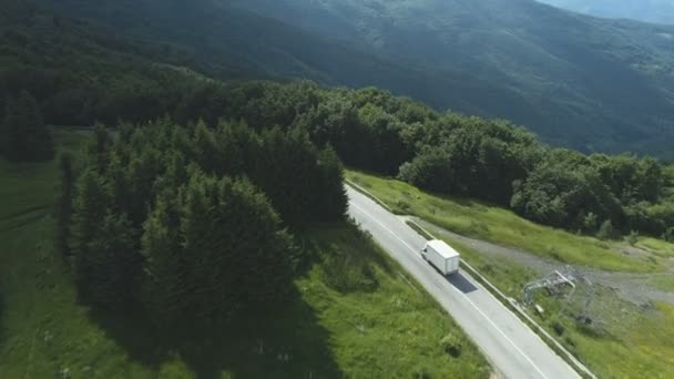 Drone following white cargo van driving along mountain road with dense evergreen frorest — Vídeos de Stock