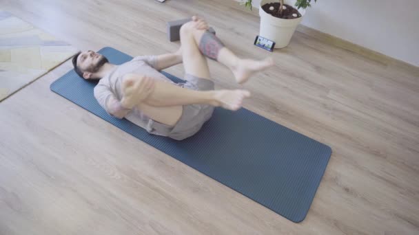 Man doing yoga on the floor practicing variation of Wind Relieving pose — Vídeo de stock