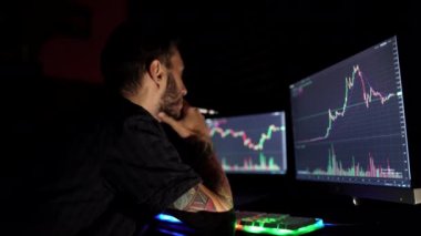 Siyah gömlekli borsacı karanlık bir monitör odasında çalışıyor. Ekranlar grafiklere bakıyor.