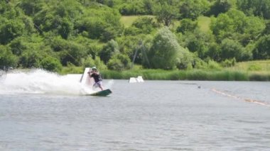 Wakeboardcu halatı tutarken yükseğe zıplıyor, ağır çekimde.