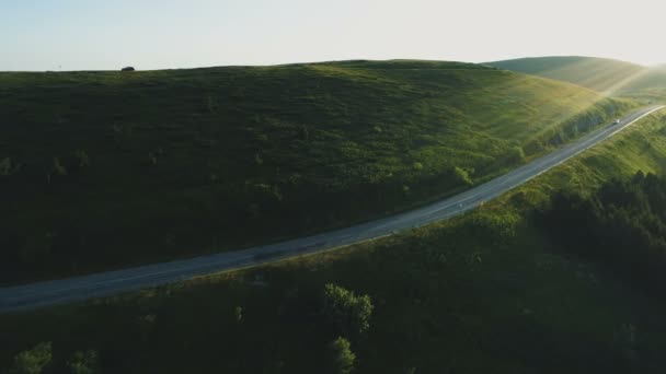 Widok z lotu ptaka czarny samochód jazdy po pięknej górskiej drodze z zielonymi wzgórzami o zachodzie słońca — Wideo stockowe