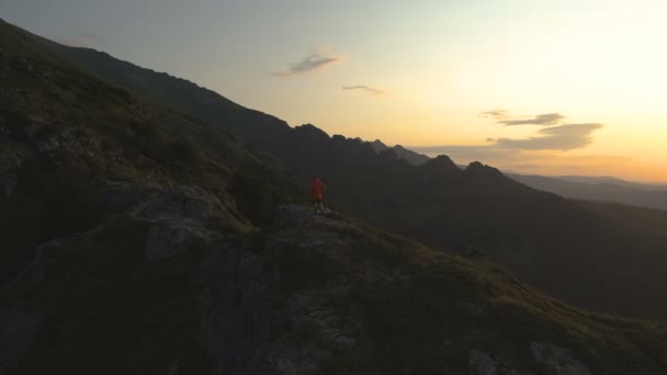 Wędrowiec cieszący się przyrodą i wolnością na szczycie góry, stojący nad skalistą przepaścią patrzący na zachód słońca — Wideo stockowe