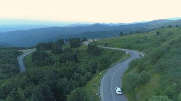 Drone follwoing twee auto 's op gebogen bergpas weg met groene vallei eronder — Stockvideo