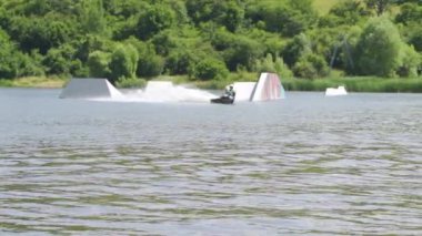 Atletik erkek wakeboardcu ters takla atıyor ve rampaların yanında başka numaralar yapıyor.