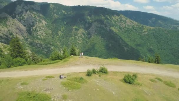 Abenteuerlustiges Paar sitzt am Bergrand. Drone Ansicht des tiefgrünen Tales unten — Stockvideo
