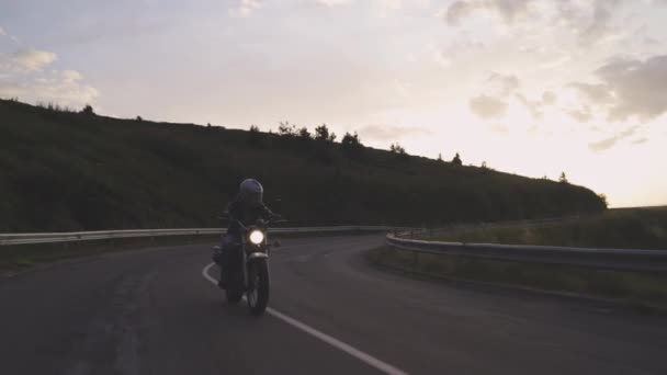 Homem andando de moto na estrada sinuosa ao pôr do sol — Vídeo de Stock