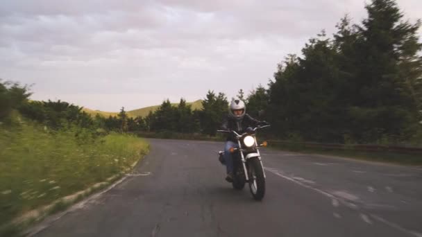Hombre a caballo motocicleta en camino sinuoso con colinas verdes — Vídeos de Stock