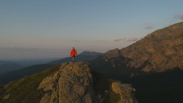 Одинокий путешественник на скальной смотровой площадке над глубоким зеленым валом, глядя на закат — стоковое видео