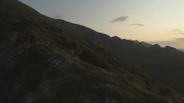Hombre de pie sobre el precipicio en las montañas mirando la puesta de sol — Vídeos de Stock