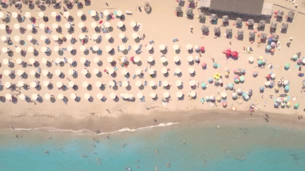 色の傘で砂のビーチのドローンビュー、海の湾の水で人々を泳いで — ストック動画