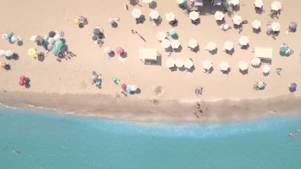 Drone vista de la playa de arena con sombrillas de color, personas nadando en el agua de la bahía de mar — Vídeo de stock