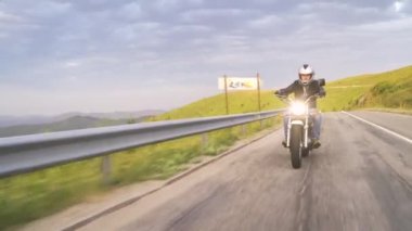 Dağ yolunda kaskı açık motosikletli. 