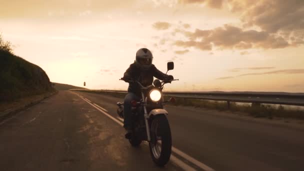 Motocicleta motociclista na estrada da montanha sinuosa ao pôr-do-sol com farol ligado — Vídeo de Stock