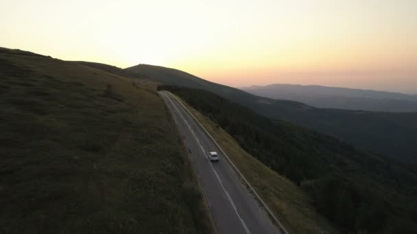 Hava aracı gün batımında yeşil tepelerde arabayı takip ediyor. — Stok video