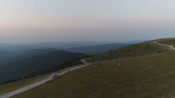 Drone segue carro dirigindo por uma estrada de passo de montanha com fundo profundo vale — Vídeo de Stock