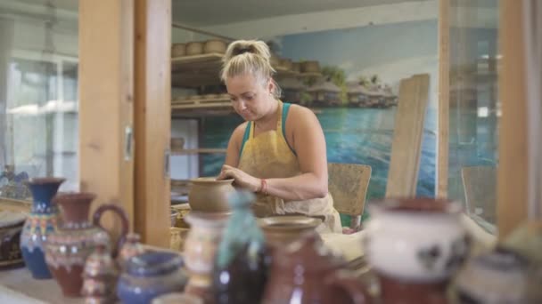 Молода жінка формує глину своїми руками створюючи глечик в майстерні — стокове відео
