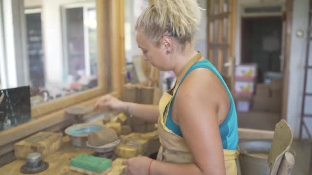 Женщина-гончар берет немного глины из ведра для работы и положить его на гончарные колеса — стоковое видео