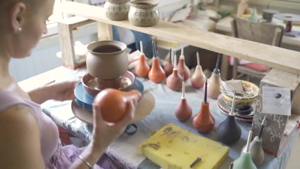 Жіночий Поттер використовує інструмент, щоб покрити глиняний горщик фарбою, працюючи в майстерні — стокове відео