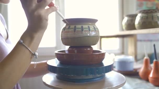 Крупним планом молода жінка малює глиняний керамічний горщик на обертовому колесі — стокове відео