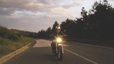 Dağ yolundaki motosikletlinin önü açık kasklı, klasik motosikletli.