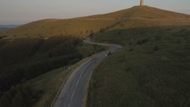 Drone a seguito di ciclista energico accelerare lungo la strada di montagna asfaltata al tramonto — Video Stock