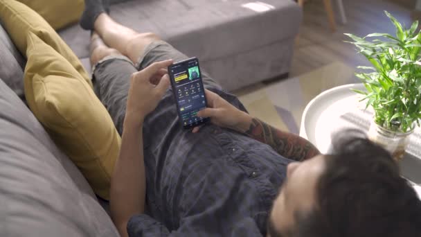 София, Болгария-07 08 2021: Человек, использующий криптовалютный кошелек на мобильном телефоне, лежа дома на диване — стоковое видео