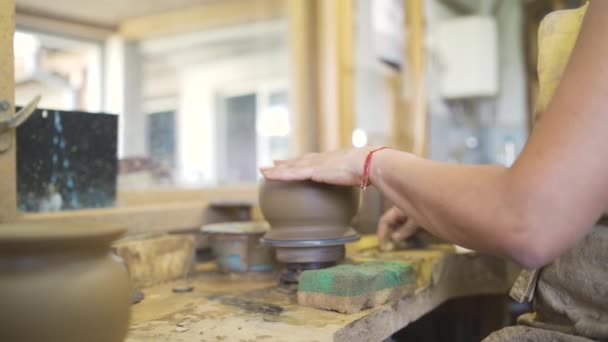 Primo piano di una giovane donna vasaio che scolpisce su una ruota vasai un vaso di argilla marrone — Video Stock
