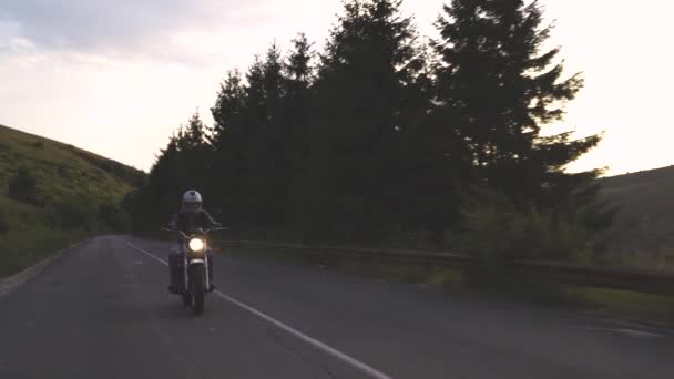 Muž s helmou na koni motocykl na venkově silnici se zelenými kopci a krásnou oblohou