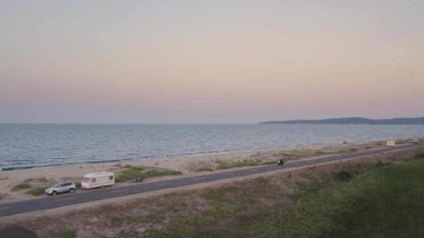 Flygfoto av svart motorcykel körning längs kustvägen med fridfull sandstrand — Stockvideo