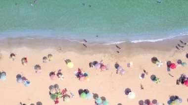 Kalabalık kumsal manzarası ve sakin masmavi deniz suyu.