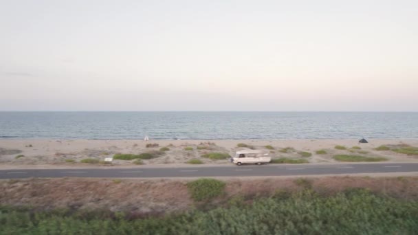 Drönare flyger bredvid tom strand väg med parkerade resande släpvagnar nära sandstrand — Stockvideo