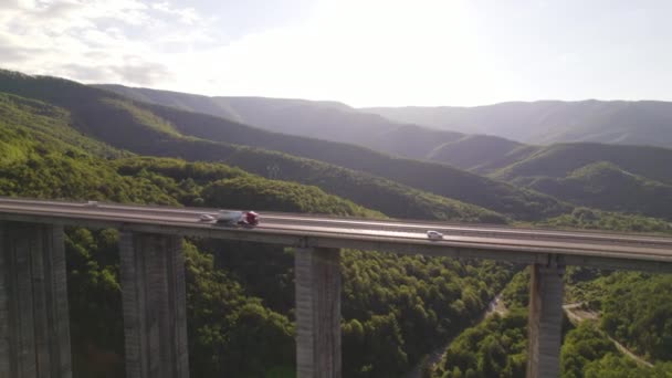 Por la noche el tráfico de camiones en el puente de la carretera contra colinas verdes y valle profundo — Vídeo de stock