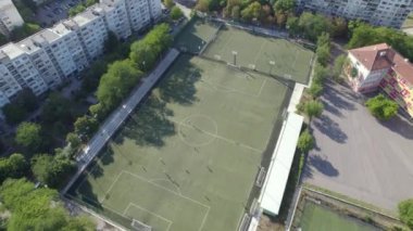Futbol sahası ve uzun ağaçlı evleri olan bir şehrin hava görüntüsü.