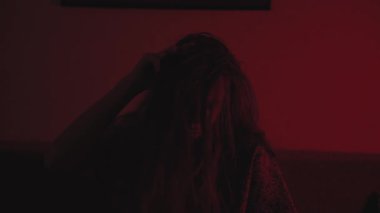A creepy mentally ill woman stands alone in a dark, abandoned room. The dim light highlights her pale face and empty eyes, creating a chilling horror atmosphere. Perfect for psychological thriller or