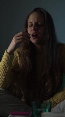 Kadın kendini hasta hissediyor ve sıcaklığını evde bir termometreyle ölçüyor. Hastalık ve kendine bakımı temsil ediyor..