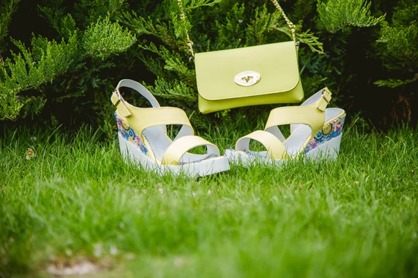 Sarı sandal ve yeşil çimenlerin üzerinde bir el çantası — Stok fotoğraf