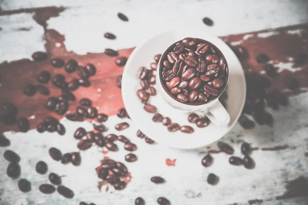 Chicchi sparsi di caffè in una tazza su uno sfondo di legno — Foto Stock