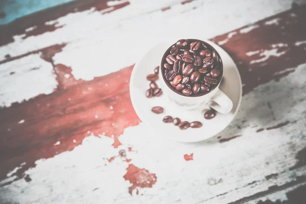 Grains éparpillés de café dans une tasse sur un fond en bois — Photo